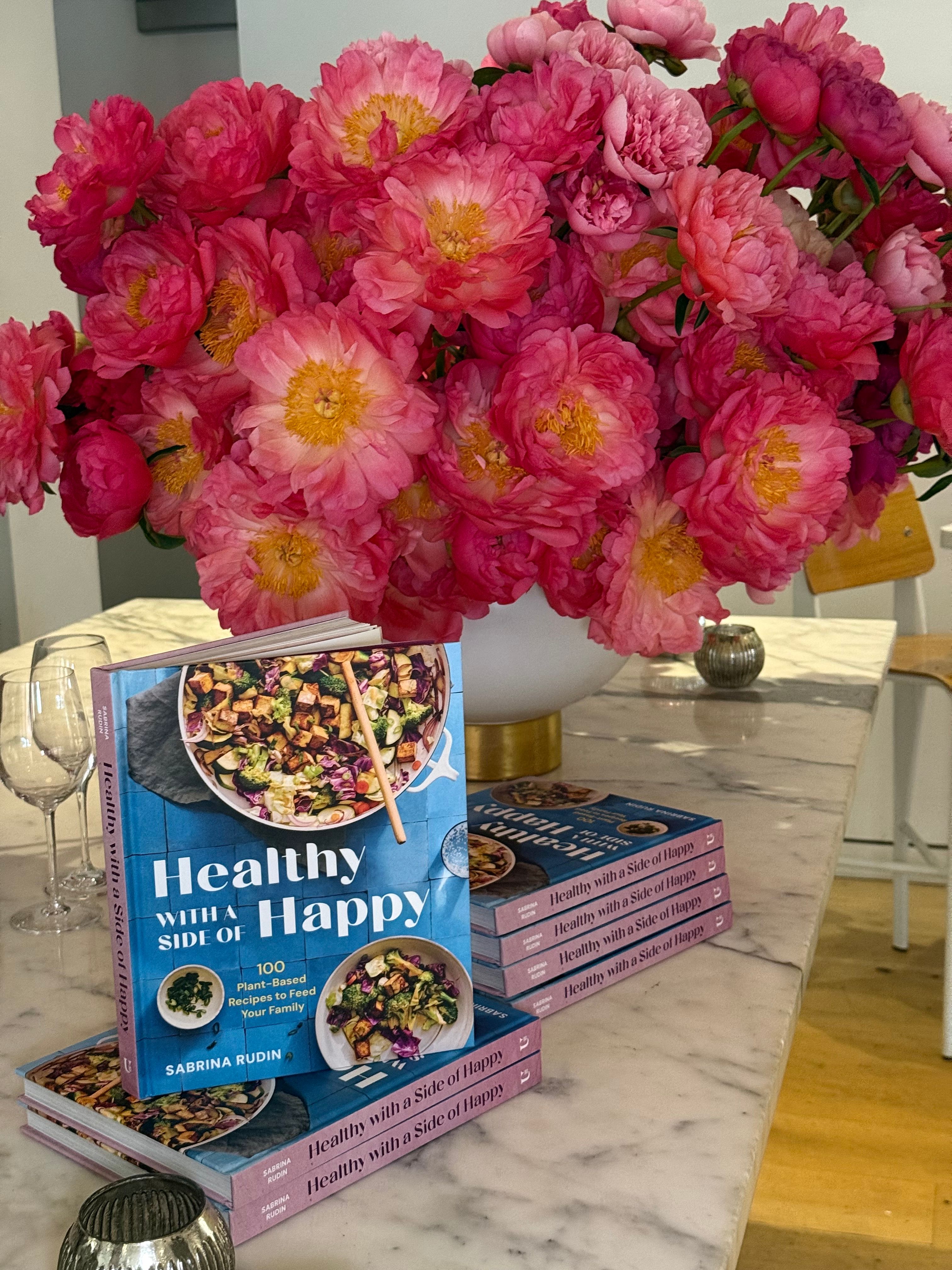 Sabrina Rudin’s Healthy with a Side of Happy cookbooks displayed with bright pink peonies at the Greenwich Village launch party.
